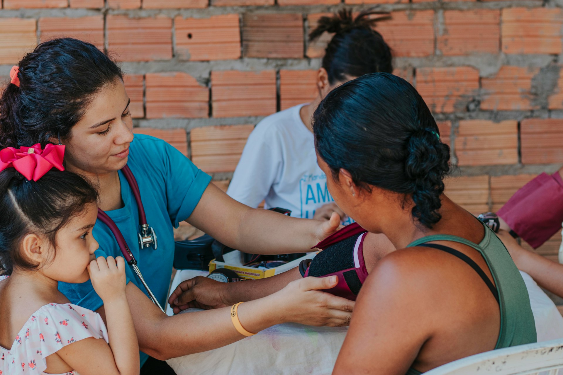 Image showing a female medical provider with blue scrubs and a stethoscope treating patients outdoors